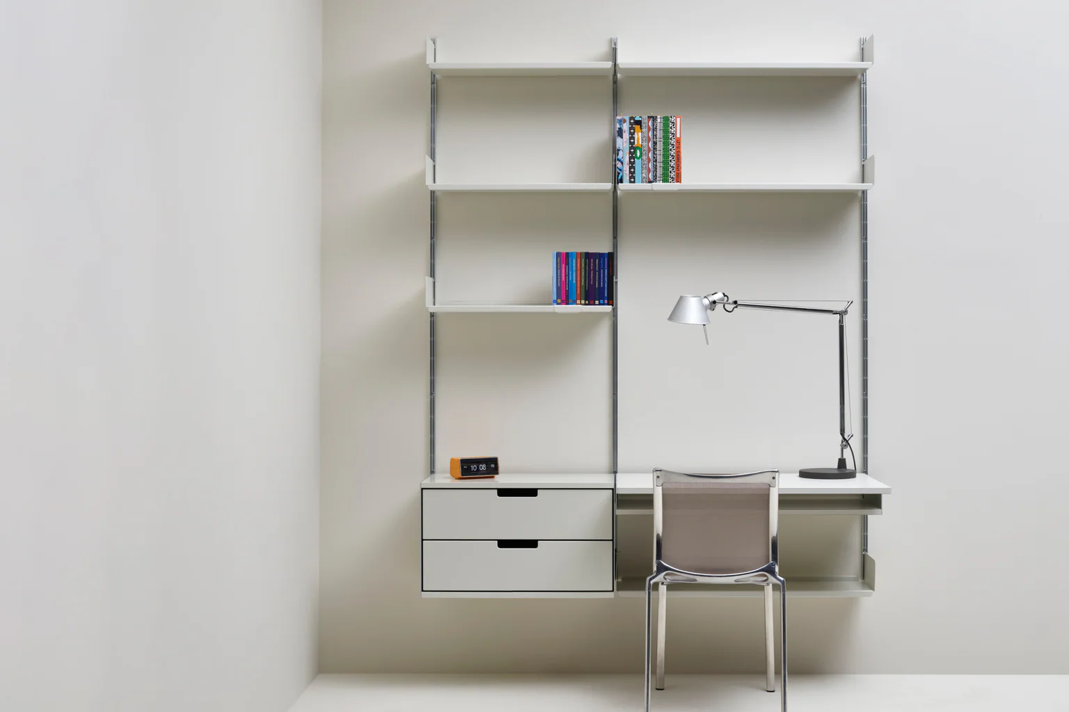 A white Vitsœ 606 shelving system configured as a desk and storage wall in a lived-in room.